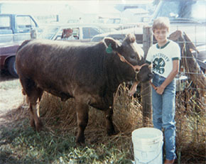 Childhood photo for Dr. Laura Beane Freeman standing next to a cow.