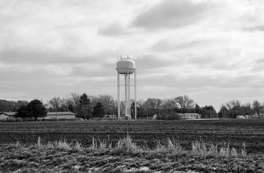 A watertower in the distance in a field.